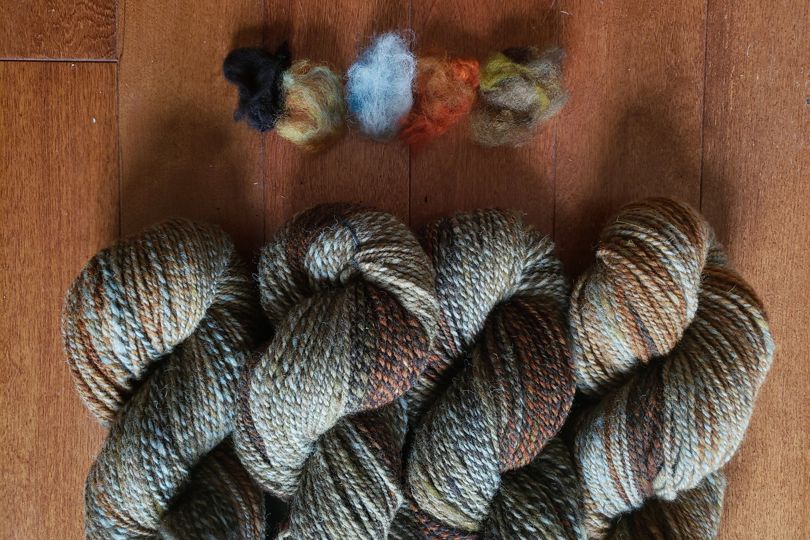 Three skeins of multicolored yarn on a wooden surface with small balls of yarn below.